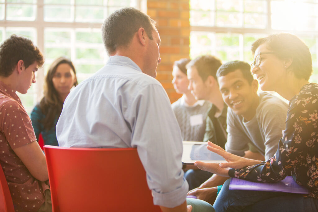Woman With Digital Tablet Speaking To Man At Group Therapy Session